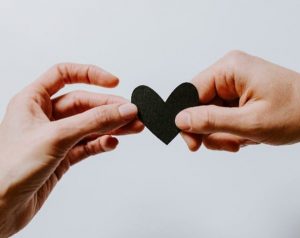 Two different people's hands holding a black paper cut out heart