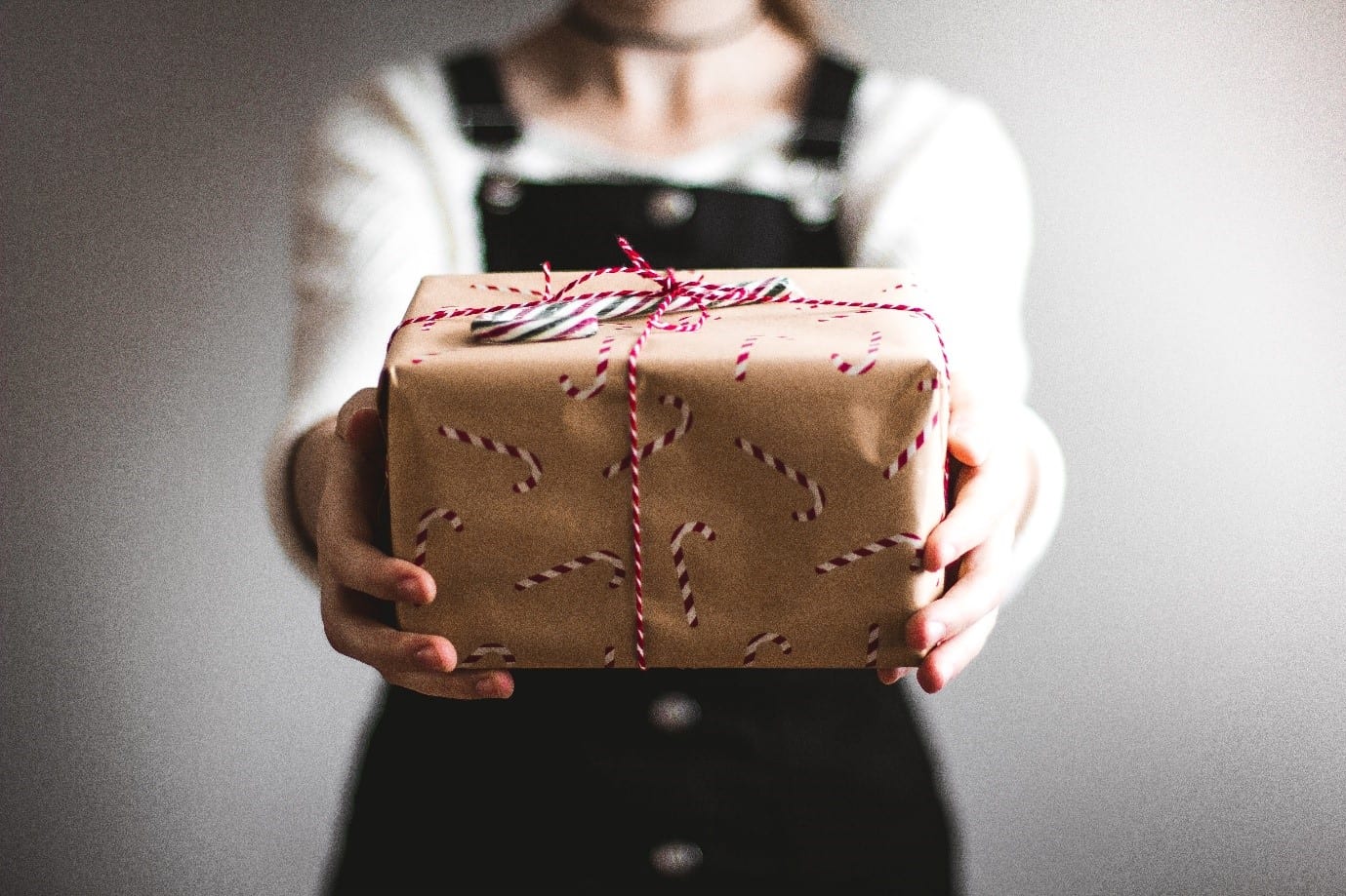 Person holding a christmas gift wrapped in brown paper with red ribbon