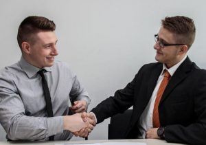Two men wearing suits shaking hands and smiling at each other